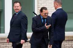 Johnny Depp bows to his fans during a recess outside court. A man behind him smirks.