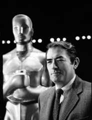 Black and white photograph of Gregory Peck standing in front of a large Oscar trophy