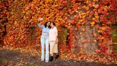 Two Cornellians take a selfie in front of a wall of leaves.