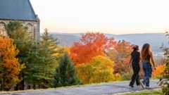 Two Cornellians walk along the path at the top of the Cornell University Libe Slope with autumn leaves in the background.