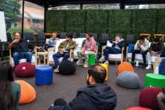 A small group of people sitting together in a room with multicolored furniture and a green foliage wall