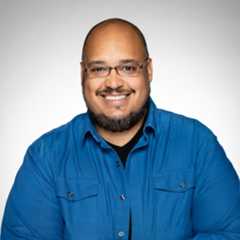 Headshot of a smiling person who is wearing a blue shirt in front of a white backdrop