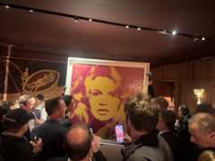 Crowd surrounding an Andy Warhol artwork of Brigitte Bardot at an auction preview, with collectors photographing the vibrant pop-art portrait.
