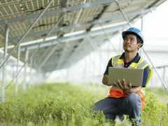 Increase Solar Power Production and Performance by using Cloud-based Monitoring. Solar service technician use a laptop computer under a solar panels module to access logs data of equipment to troubleshoot in a solar power plant.