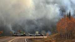 Large wildfire smoke cloud over fire response trucks parked on a road