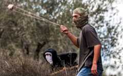 A masked Jewish extremist swings a slingshot while hurling stones at Palestinians who had gathered for the annual olive harvest season, during an attack by Israeli settlers on the Palestinian village of Beita, south of Nablus in the West Bank, on October 10, 2025. (Photo by Jaafar ASHTIYEH / AFP) A masked Jewish extremist swings a slingshot while hurling stones at Palestinians who had gathered for the annual olive harvest season, during an attack by Israeli settlers on the Palestinian village of Beita, south of Nablus in the West Bank, on October 10, 2025. (Photo by Jaafar ASHTIYEH / AFP)