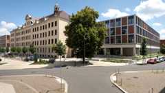 Ein saniertes Altbaugebäude und ein Neubau die miteinenander verbunden sind. In der Mitte der beiden Gebäude steht ein Baum