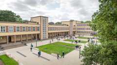 Seitlicher Blick auf ein Schulgebäude sowie den Schulhof mit grüner Wiese in der Mitte Hofansicht Schule am Palmengarten