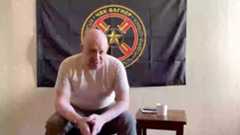 A screenshot from a video interview with Mr. Prigozhin posted to social media. Mr. Prigozhin is sitting in front of a flag that has a logo of the Wagner private military group.