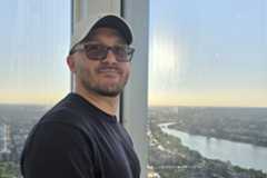 Cristiano Fanelli stands at a window that overlooks a city and river.