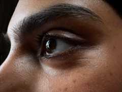 A woman in an empty room being photographed. The side face of women is zoomed in focused on eyes, The Photo app toggles through the focal lengths to demonstrate the capabilities of the pro camera system, showcasing: Macro