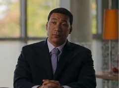 Man sitting with dark jacket and purple tie.