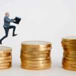 A man leaps from a stack of gold coins to the next, each one higher than the last.