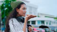 woman with headphones speaking into speaker of phone