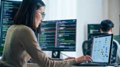 Woman reviewing three monitors with code and process flow