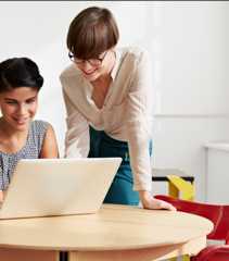 ノートパソコンの前で作業をしている二人の女性。一人は椅子に座っており、もう一人は立ちながらパソコンの画面を見ている。