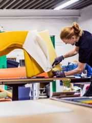 黒いTシャツを着て作業手袋をしたイケアコワーカーが、鮮やかな黄色の布地でパーソナルチェアを張り替えている。