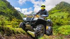A man on a quad bike by green mountains.
