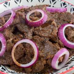 Filipino beefsteak with onions in a white serving bowl.