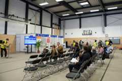 Ankommenszentrum Leipzig In der Halle des Ankommenszentrums sitzen Menschen auf aufgereihten Stühlen vor den Schaltern.