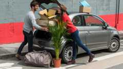 Umzug mit Auto Eine Frau und ein Mann laden Umzugskartons in ihr Auto. Davor steht eine Zimmerpalme.