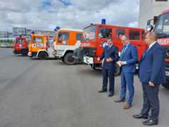 Hilfskonvoi Ukraine Drei Männer stehen vor mehreren Lkws und Feuerwehr-Fahrzeugen.