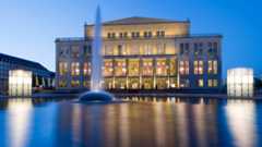 Oper Leipzig- Außenansicht blaue Stunde mit Brunnen Außenansicht der Oper Leipzig zur blauen Stunde mit einer flachen Wasserfläche und einer Wasserfontäne davor.