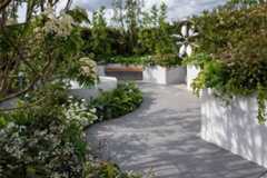 Wide path of Anthracite Porcelain Large Patio Slabs curves round central raised pond bordered by green and white planted bed.***Designed by KarenTatlowGardenDesign.co.uk | Built by DesignItLandscapes.co.uk & MjlDesign.co.uk