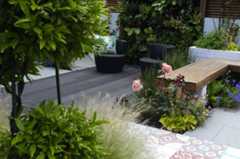 Charcoal composite outdoor decking laid with decorative tiles in garden with topiarised laurel, living wall and brick raised beds.***Botanica Gardens, www.botanicagardendesign.com