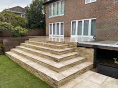 Frosty Grey 16mm Porcelain Paving used for patio and steps with mixed stone cladding in tiered garden layout.***S & D Paving