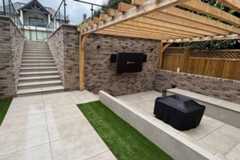 Outdoor entertainment space beneath a timber pergola, finished with Grey York Porcelain Paving and built-in seating.***Bjorn Build