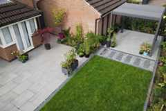 Kandla Grey 16mm Porcelain Paving used in a modern garden patio with outdoor furniture and lawn, by SP Landscapes.***SP Landscapes