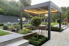 Lit up proteus grey pergola sits on platinum grey porcelain paving with lawn and flowerbeds surrounding.***The Landscape Design Studio