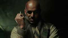 Raza glares while holding a cigarette