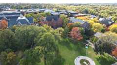 Drone view of campus during fall. The drone captured the Great Lawn and the flagpole with the U.S. flag and the UN flag. Tree leaves are just starting to turn from green to orange.