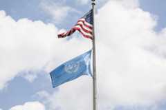 The United States flag and the UN flag fly high against a blue sky
