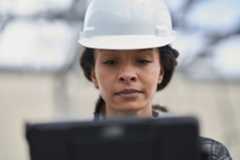 Field engineer wearing hard hat looking at laptop screen.