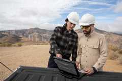 Two people, outside, looking at a laptop that is sitting on an open truck bed.