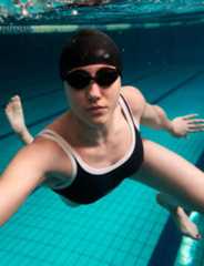 Naine ujumismütsi ja prillidega sooritab harjutust basseinis vee all.