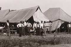 A group of men stand outside tents of various sizes.
