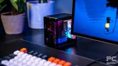 The Pironman 5 Max case sitting on the desk slightly hidden behind the monitor. In the foreground is an out of focus keyboard, and two plant pots in the back out of focus.