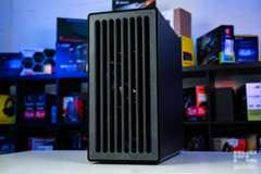 A shot of the fron of the HAVN BF 360 Flow case on a white table with a background of PC component boxes on a bookshelf. It has a faux stone looking design with vertical slits for airflow.