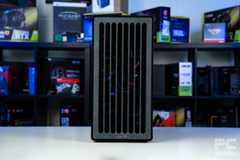 A shot of the fron of the HAVN BF 360 Flow case on a white table with a background of PC component boxes on a bookshelf. It has a faux stone looking design with vertical slits for airflow.