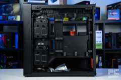 The left side open of the HAVN BF 360 Flowstanding on a white table infront of a bookshelf of PC component boxes. It shows the various stroage sleds, cable cahnnels and features of the case.