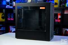 The HAVN BF 360 Flow case sitting side on with the right galss panel facing us. It sits on a white table with a background of PC component boxes on a bookshelf.