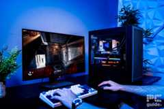 The HAVN BF 360 Flow case on a table with a build inside. Next to it is a keyboard and mouse with hands using them to play Indiana Jones on the monitor. The background is a blue wall, with two plants on either side.