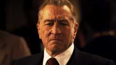 Robert De Niro's Frank Sheeran stands in a dark room in The Irishman