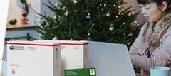 A woman preparing to ship holiday gifts with a Priority Mail Express box and a Priority Mail box.