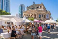 Menschen genießen das sommerliche Opernplatzfest vor der Alten Oper in Frankfurt. Zelte, Sitzbänke und Stände schaffen ein lebendiges Ambiente.